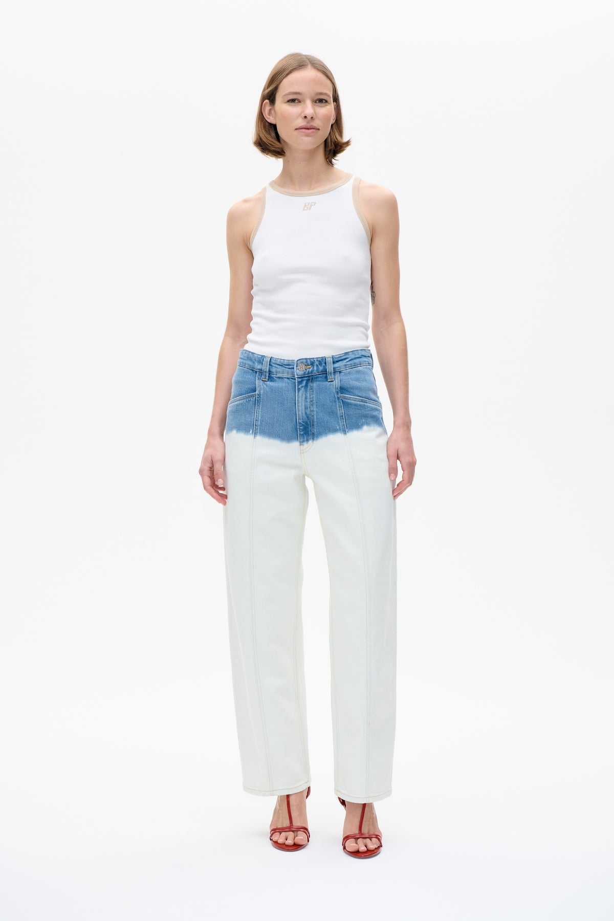 Model trägt ein weißes ärmelloses Top mit beiger Einfassung und kleinem BP-Emblem, dazu weit geschnittene Jeans mit Farbverlauf von blau zu offwhite.