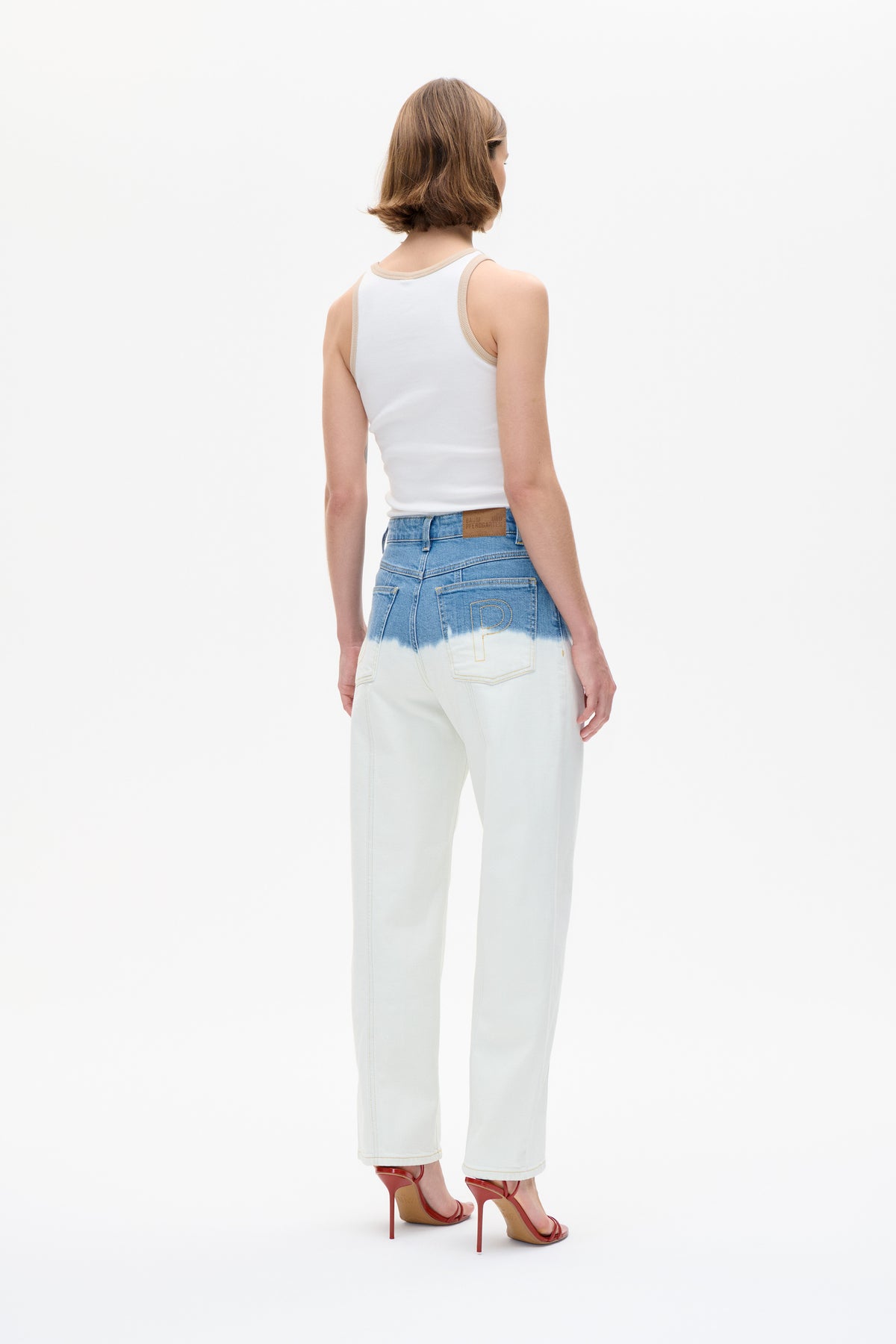 Achteraanzicht van een model in een witte tanktop met beige bies en wijdvallende jeans in twee tinten blauw en crème.