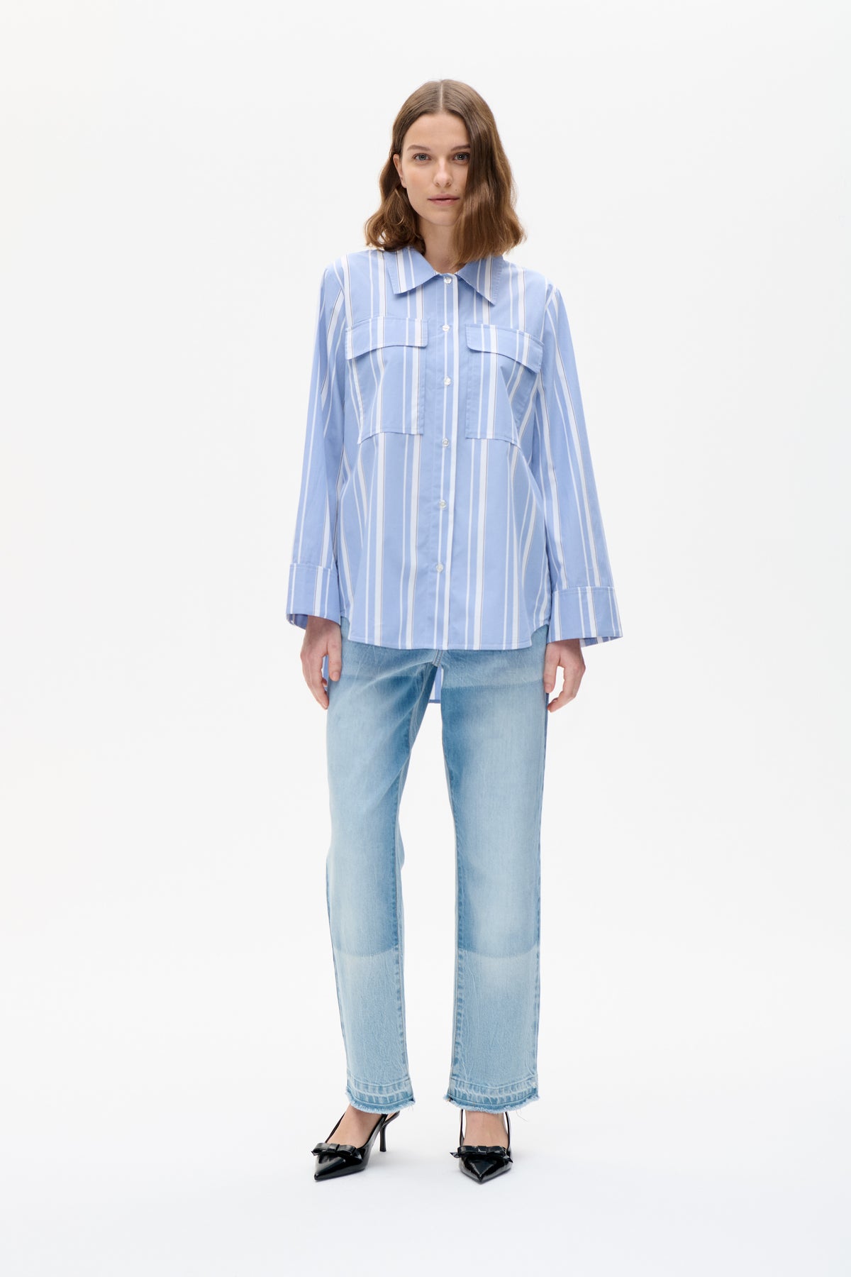 Model wearing a blue and white vertically striped button-up shirt with a pointed collar and flap chest pockets, paired with light-wash jeans.