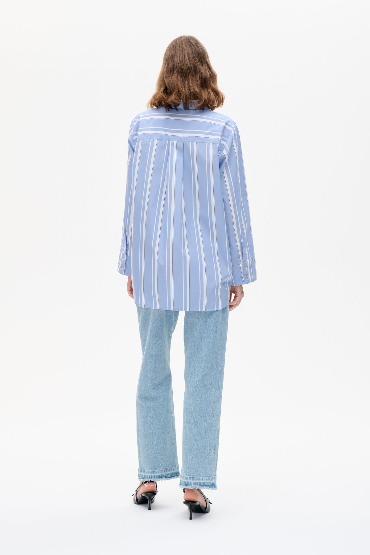 Back view of a long-sleeved, light blue shirt with white vertical stripes and a horizontal striped yoke, worn with light-wash jeans.