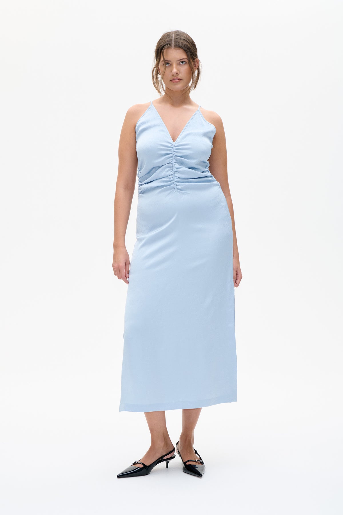 Front view of a model wearing a light blue sleeveless midi dress with a deep V-neck and ruched center front.