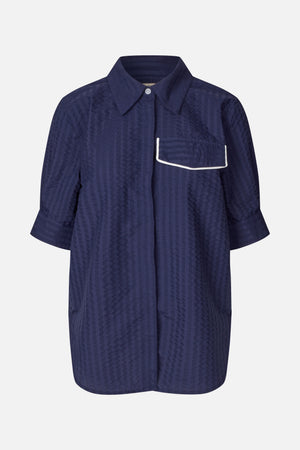 Vue de face d'une chemise à col bleu marine foncé, à manches courtes, avec un motif géométrique ton sur ton discret et une poche poitrine bordée d'un passepoil blanc.