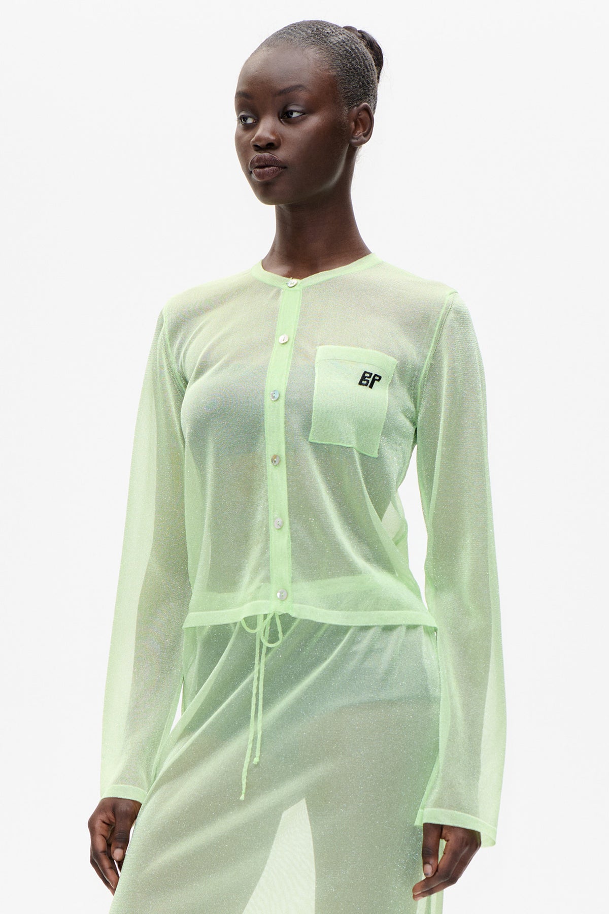 Model wearing a sheer pale lime-green long-sleeved cardigan with contrast trim and a chest pocket, shown from the front.