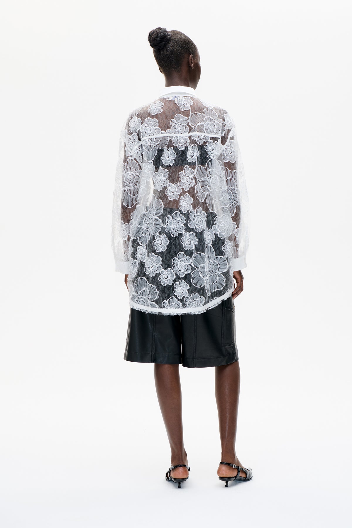 Back view of a sheer white floral lace shirt with a solid white collar and cuffs, styled over black shorts.