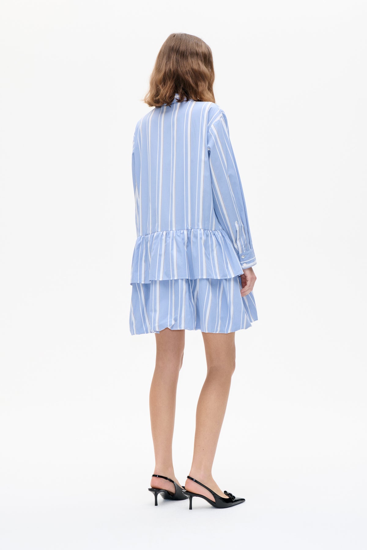 Rückenansicht eines Models, das eine hellblau-weiß vertikal gestreifte, langärmelige Bluse mit Schößchen und passenden Shorts trägt.