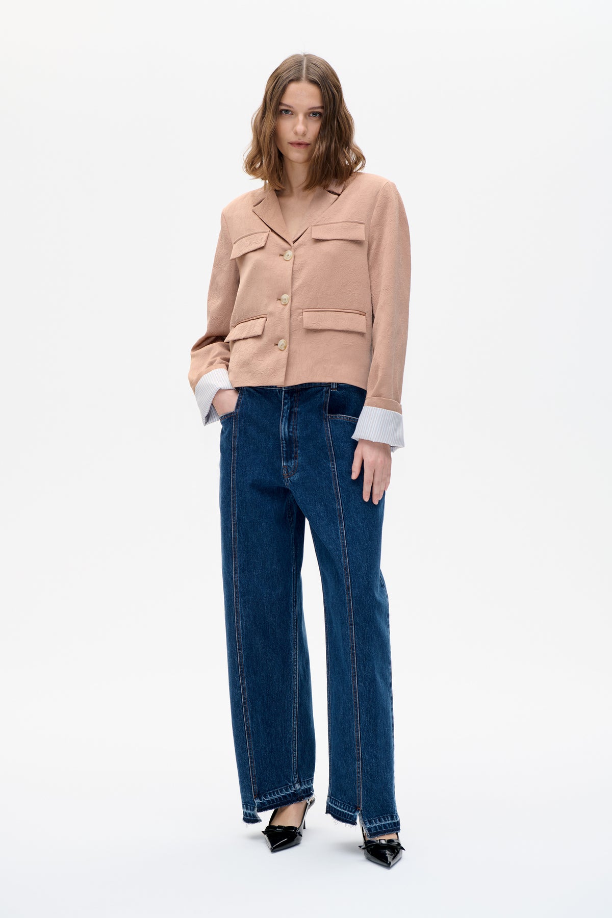 Model wearing a blush pink textured blazer with notched lapels and flap pockets, paired with wide-leg dark blue jeans.