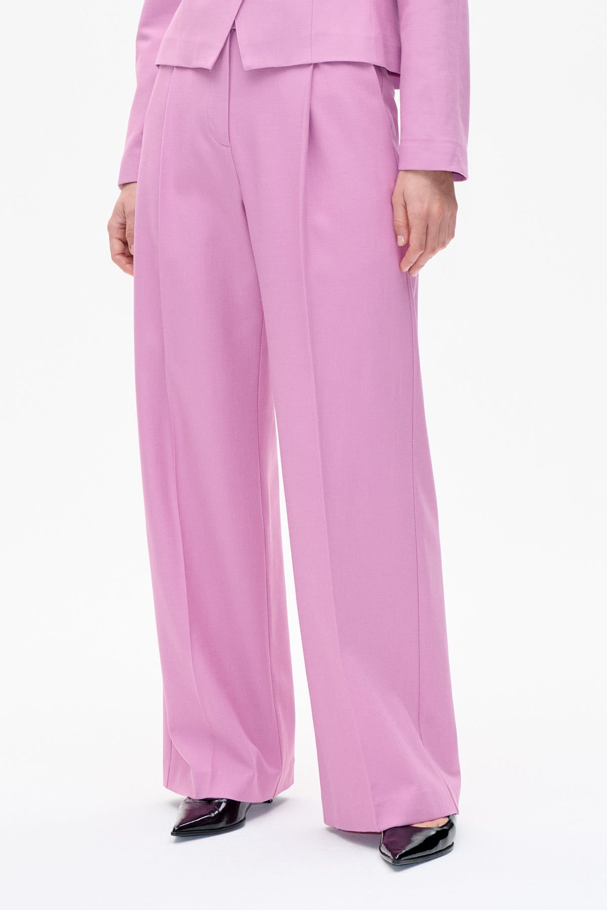Close-up front view of lilac wide-leg trousers with pressed creases, styled with a matching jacket and black pointed shoes.