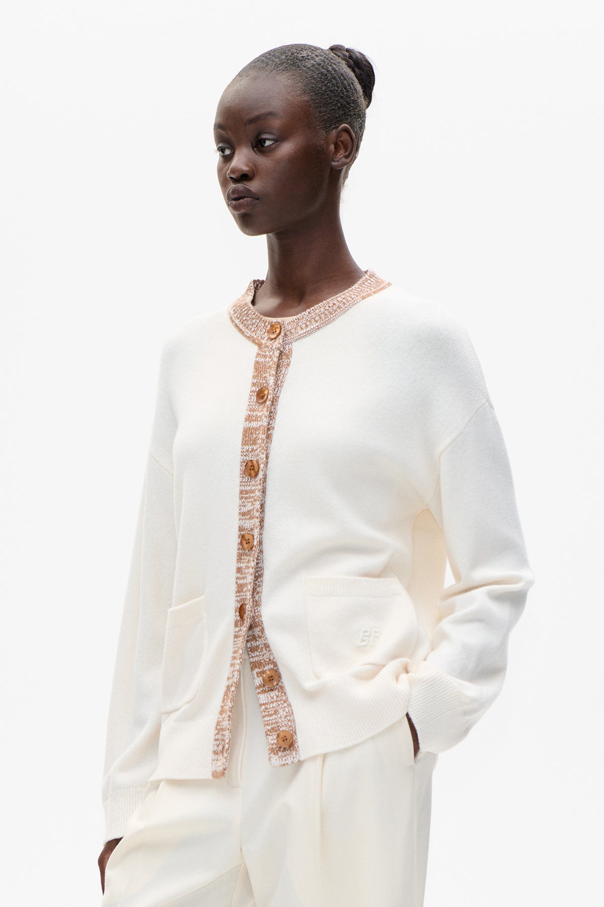 Model wearing an ivory knit cardigan with tan-and-cream patterned trim, brown buttons and front patch pockets
