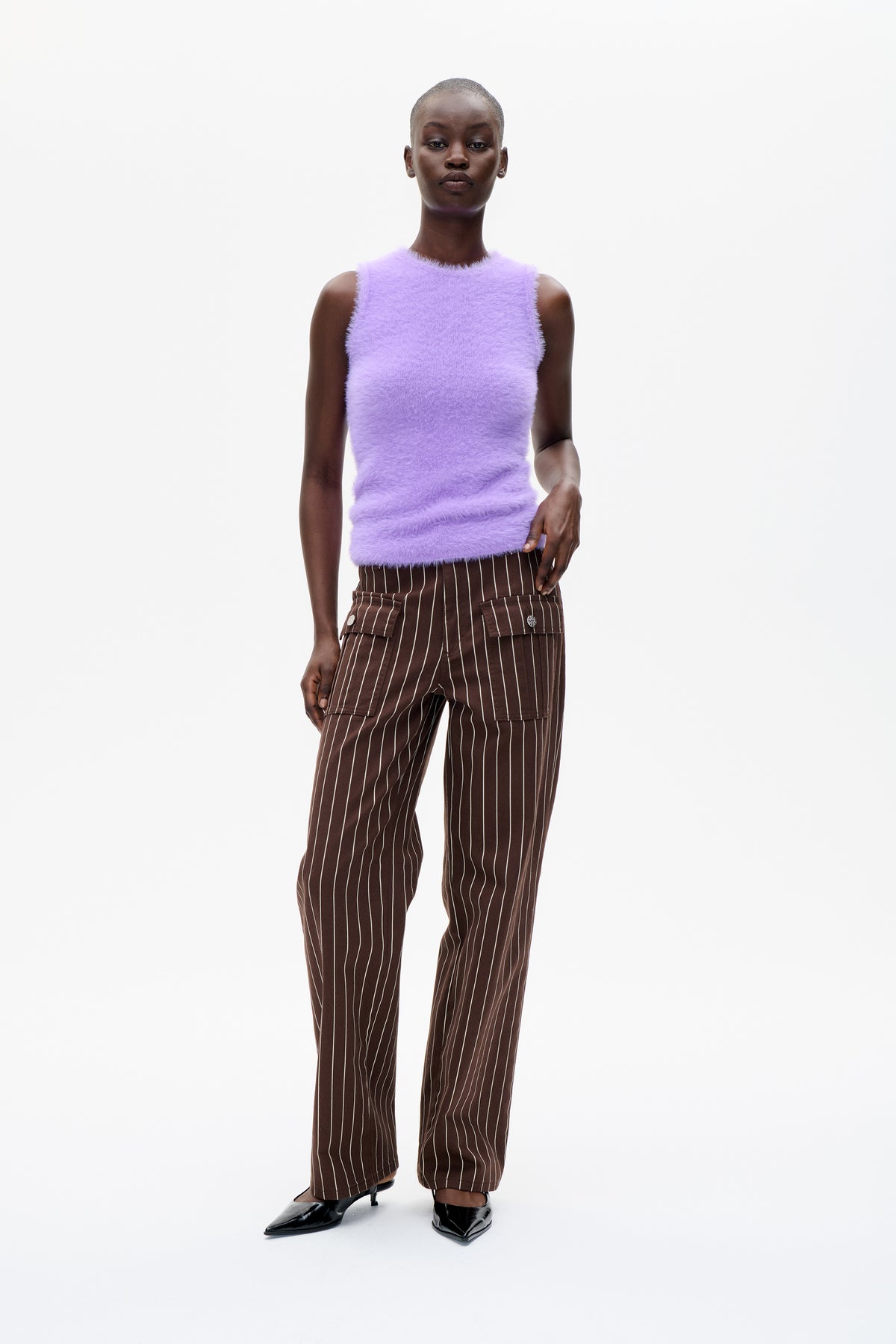 Vooraanzicht van een model in een zachte lila mouwloze top en een bruine cargo-broek met crème krijtstrepen.