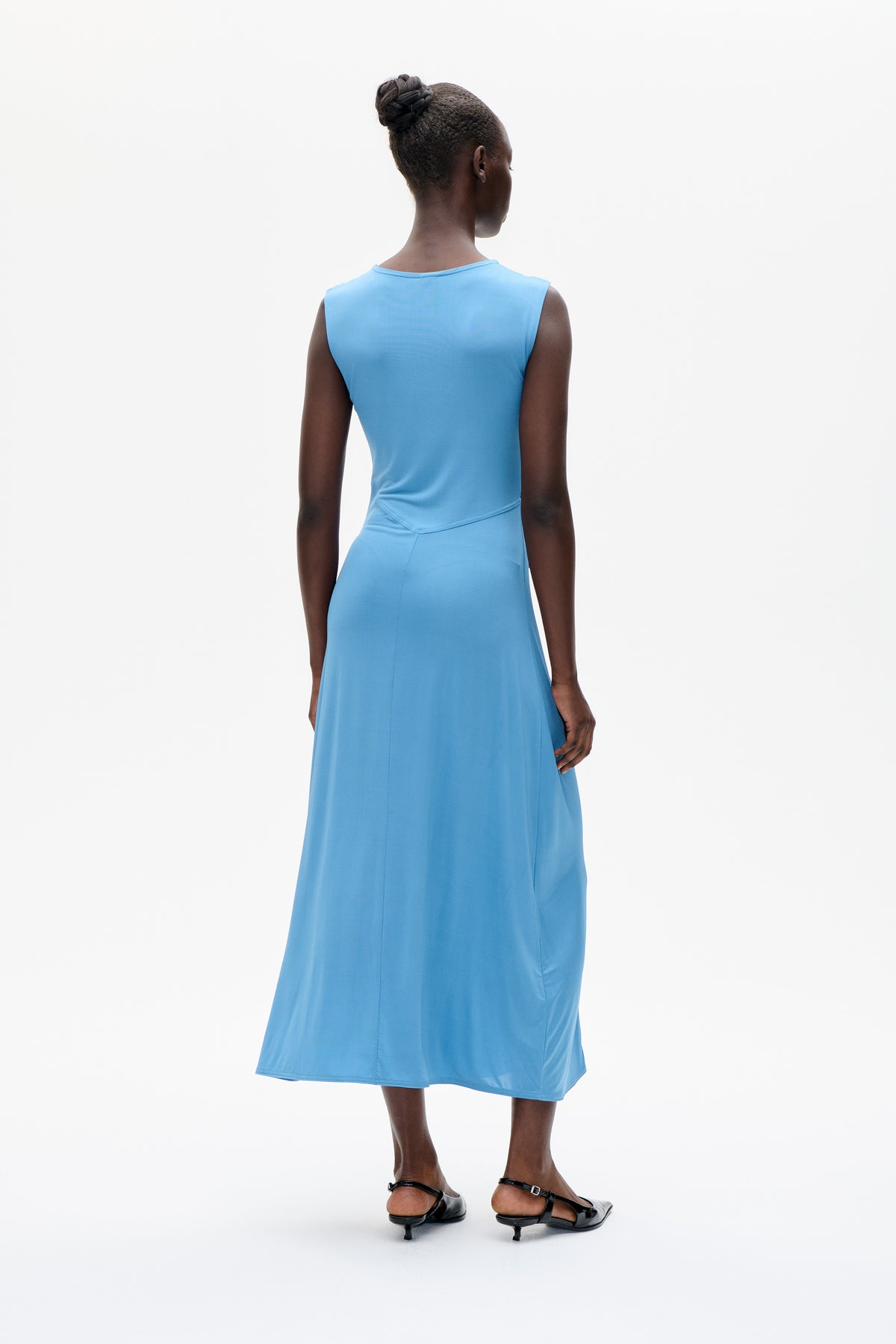 Model van achteren in een mouwloze midi-jurk in luchtblauw met een schuine taillenaad en een uitlopende rok.