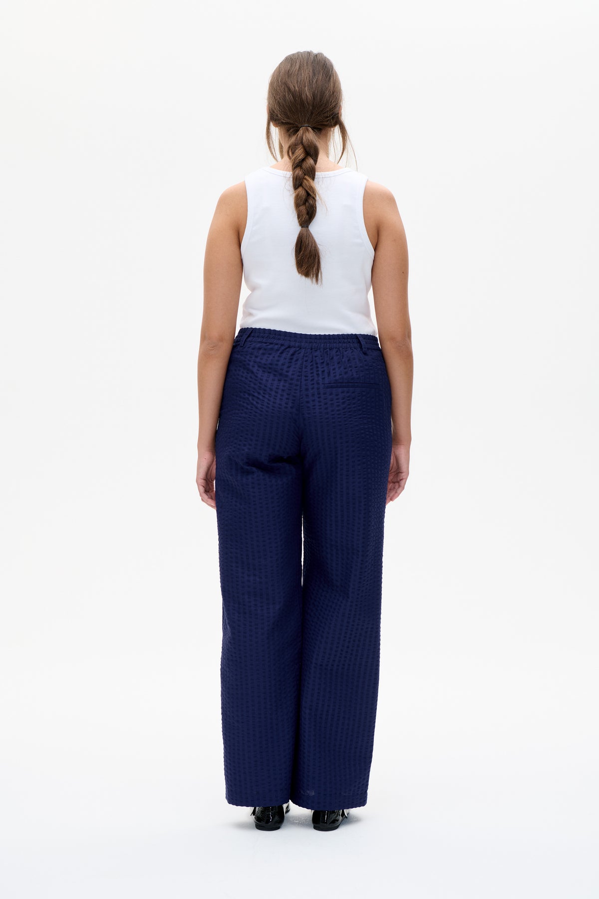 Rückenansicht eines weißen ärmellosen Tops, kombiniert mit einer marineblauen, weit geschnittenen Hose mit elastischem Bund und dezentem Strukturmuster.