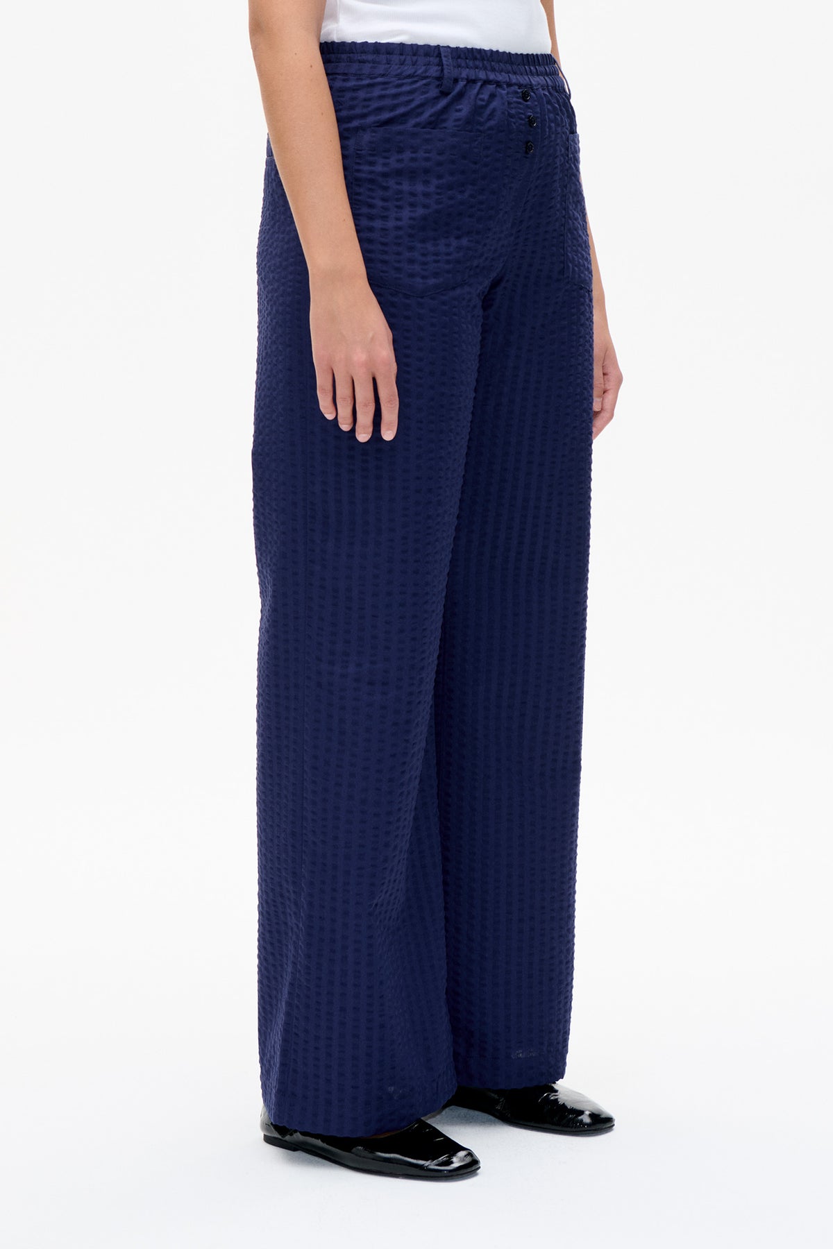 Nahaufnahme, Vorderansicht einer marineblauen, weiten Hose mit erhabenem Strukturmuster, gerafftem Bund und vorderer Knopfleiste, kombiniert mit weißem Oberteil.
