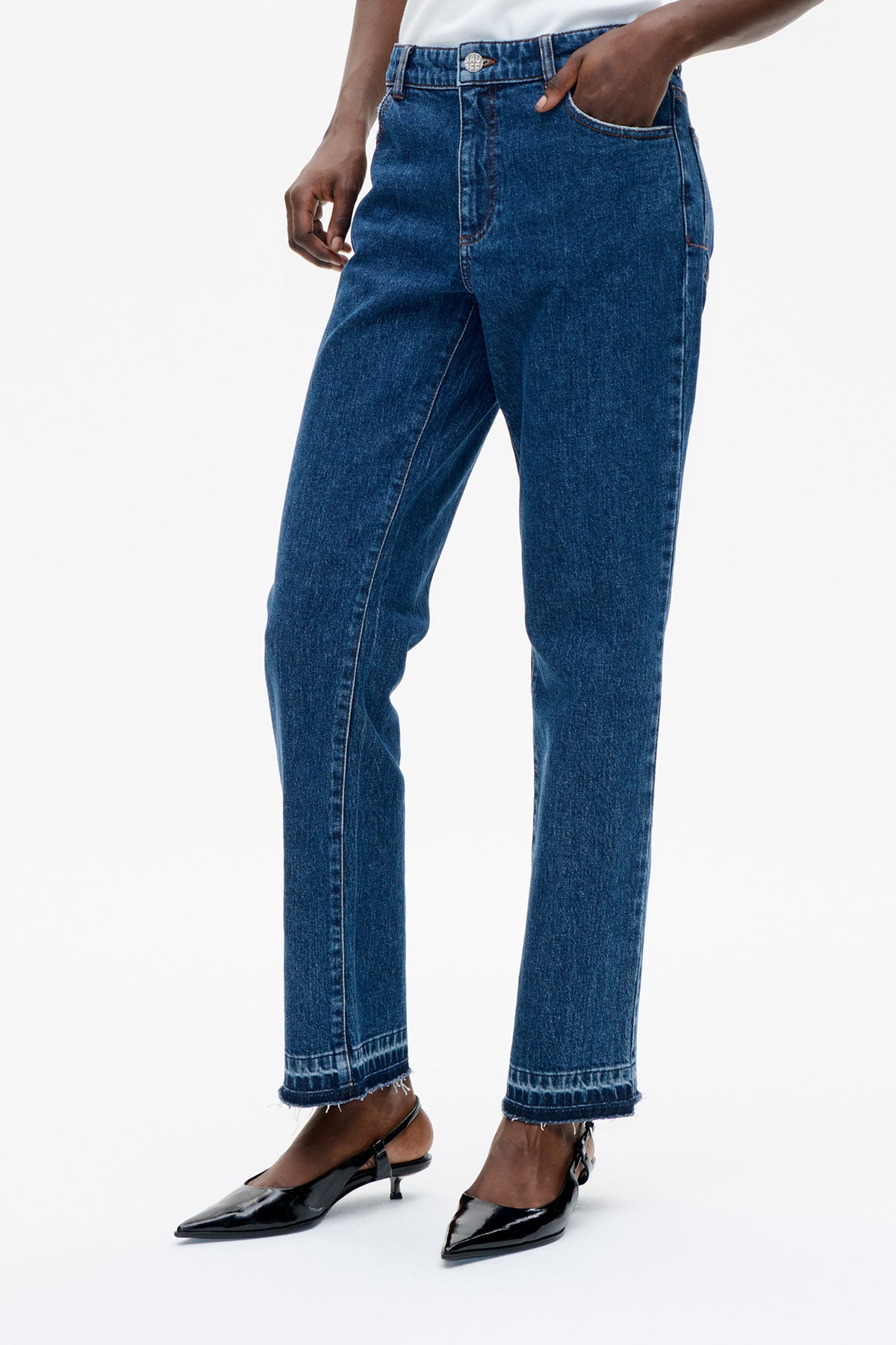Nahaufnahme, Vorderansicht: dunkelblaue, gerade geschnittene Jeans mit Kontrastnähten, Knopfbund und ausgefransten, gekürzten Säumen.
