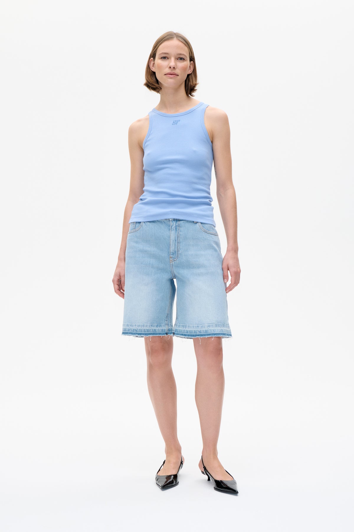 Front view of a model wearing a light blue sleeveless top with a small chest logo and light-wash denim shorts with a frayed hem.