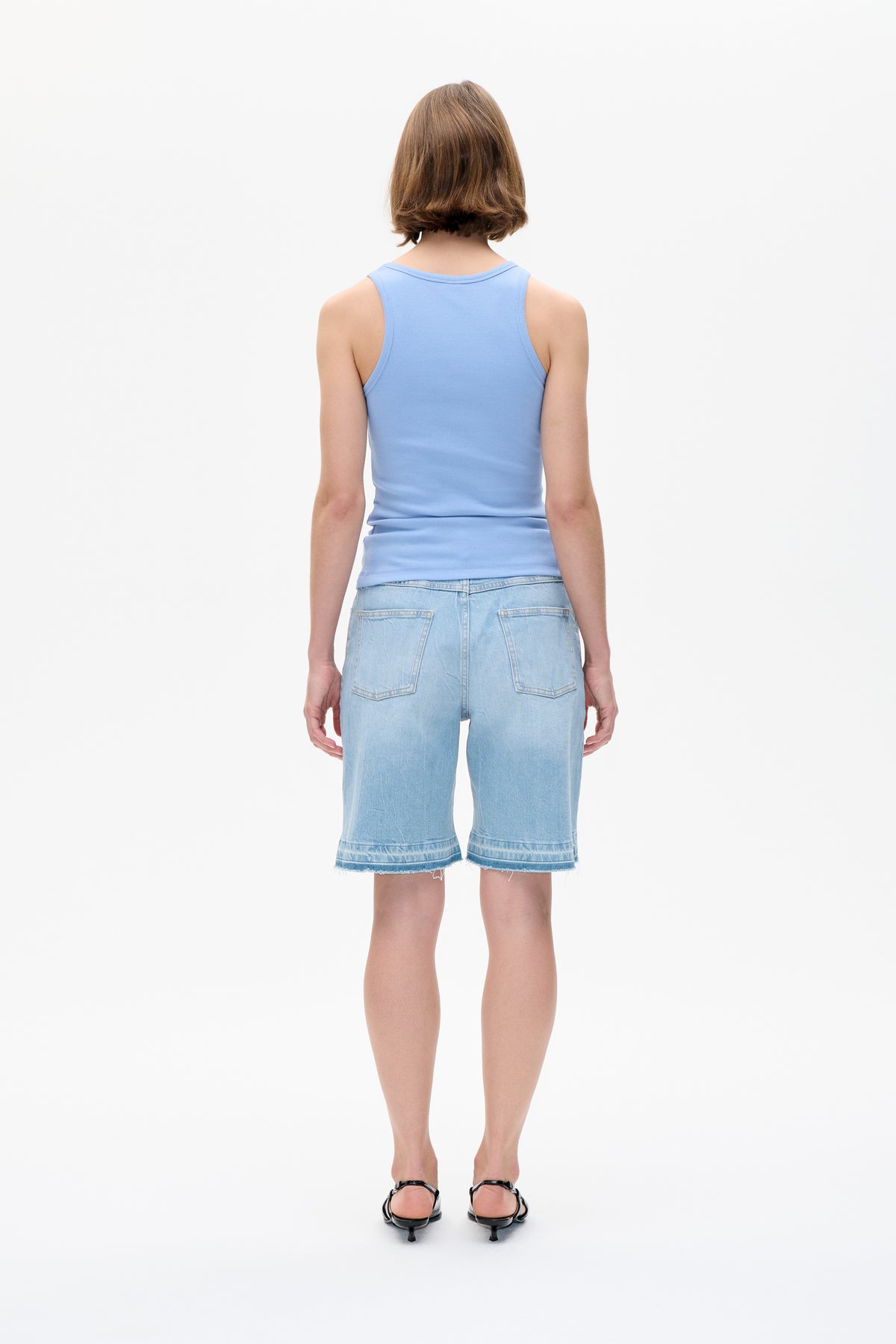 Achteraanzicht van een lichtblauwe ribgebreide mouwloze top, gecombineerd met lichtblauwe denim shorts met opgestikte zakken en rafelige zomen.