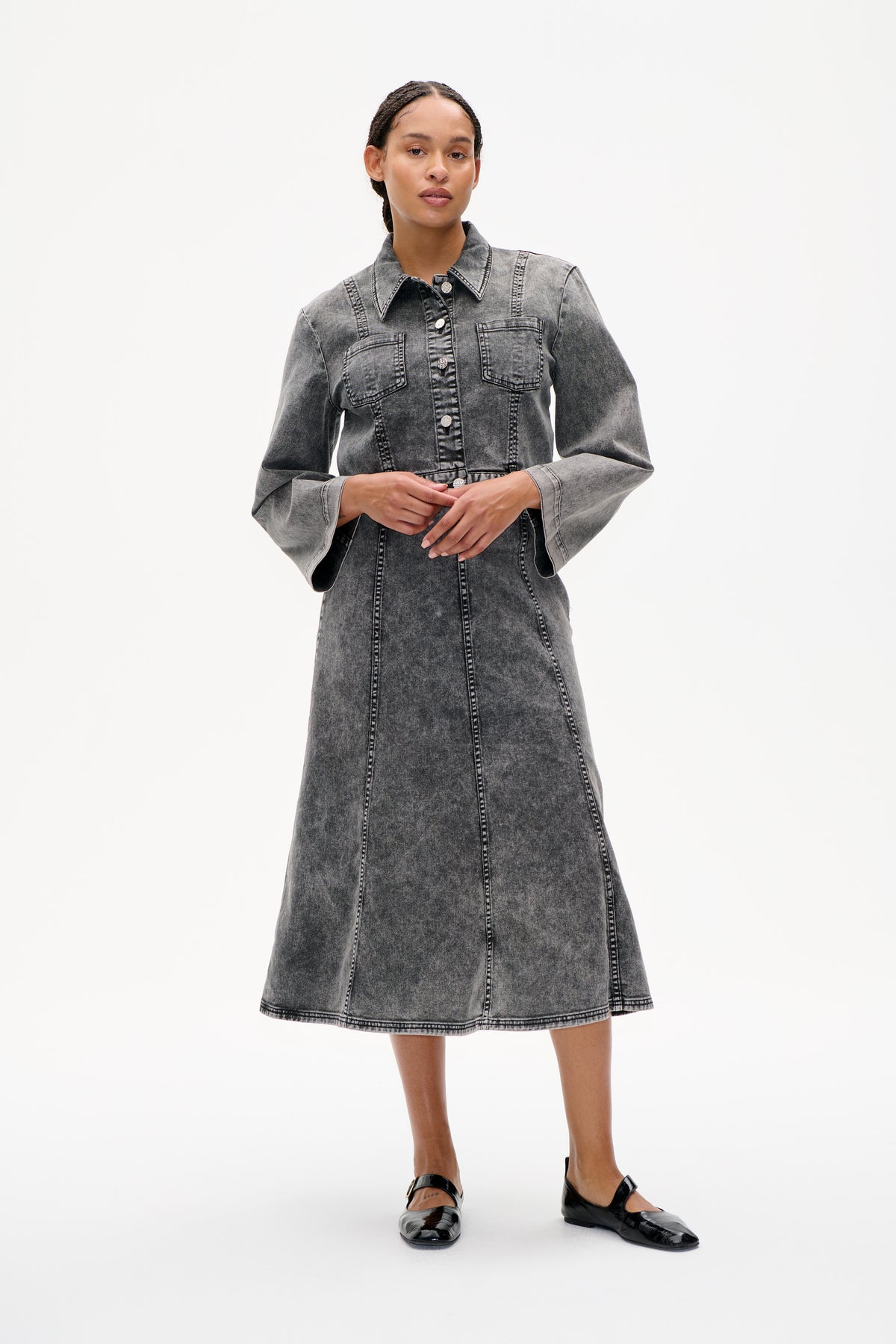 Model trägt ein graues acid-wash denim-Hemdkleid mit spitzem Kragen, durchgehender Knopfleiste, Brusttaschen und kontrastierenden Nähten, gestylt mit schwarzen Ballerinas.