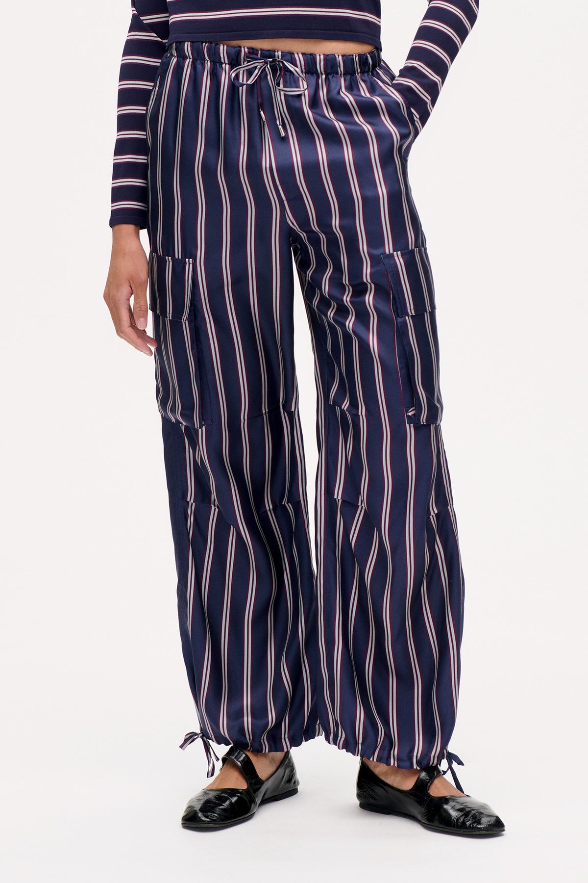 Detailaufnahme der Vorderseite einer marineblau gestreiften Cargohose mit elastischem Bund und Kordelzug, aufgesetzten Taschen und Bindebändern an den Beinabschlüssen.