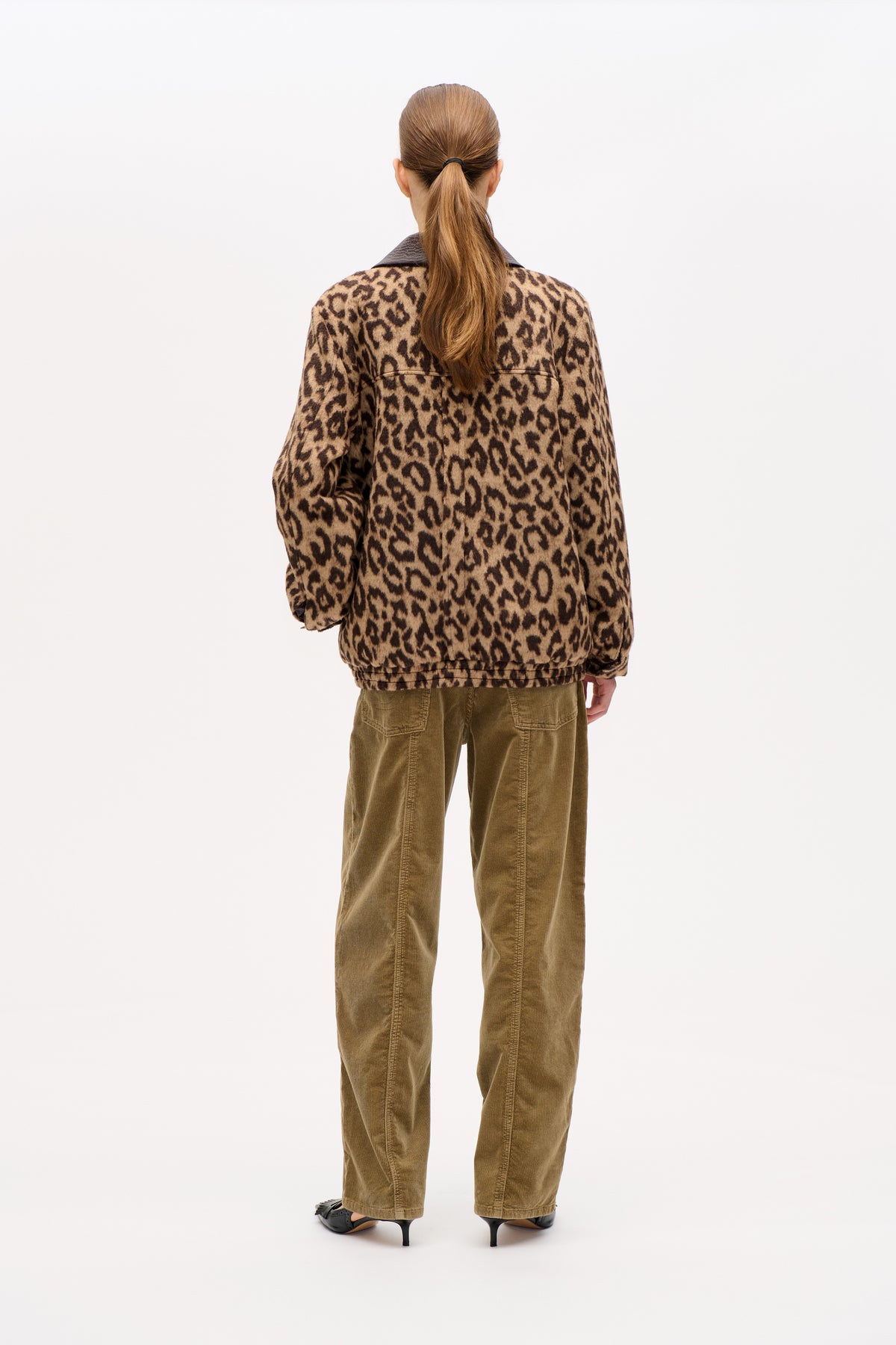 Back view of a model wearing a tan and dark brown leopard-print jacket with a dark collar and olive corduroy trousers.