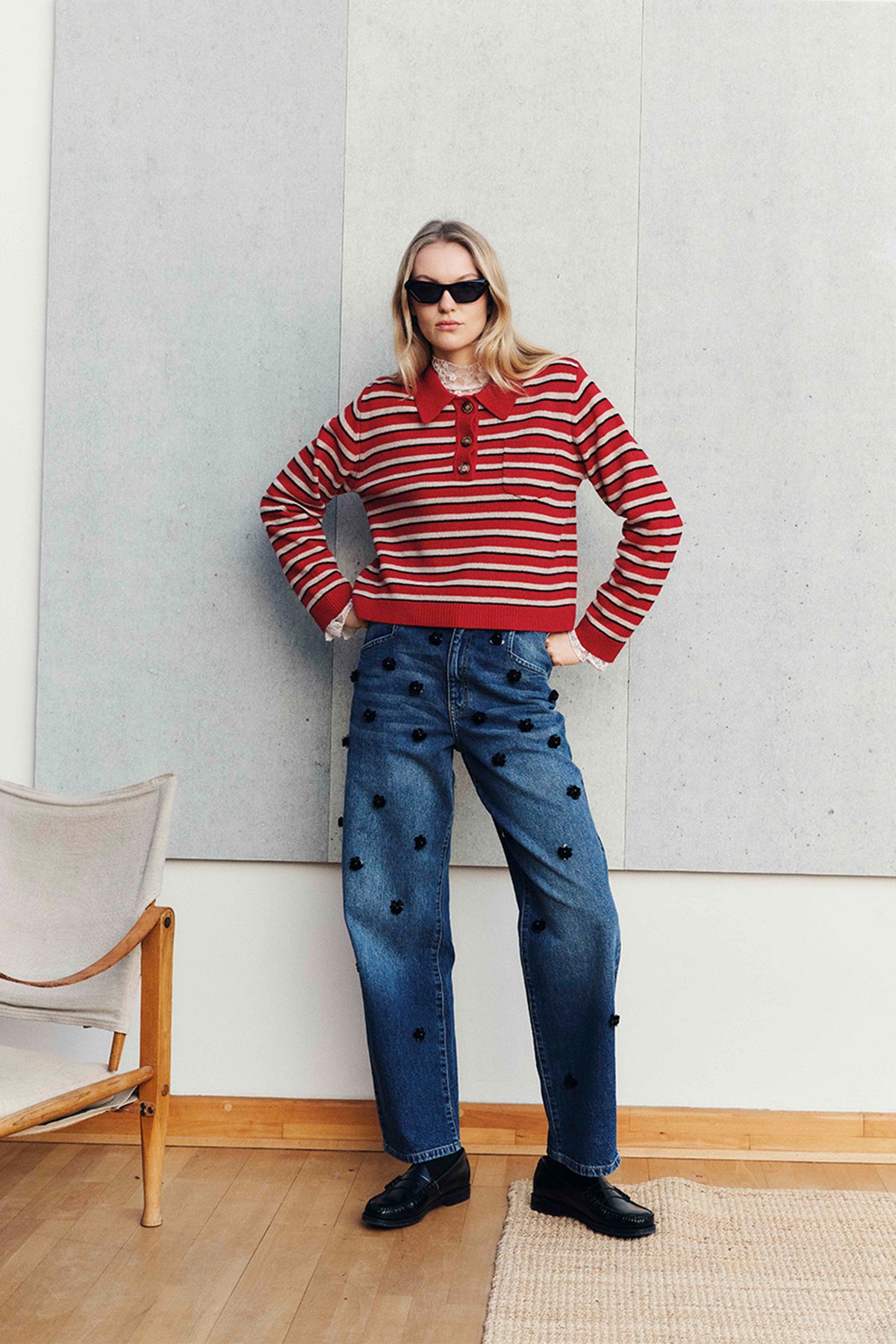 Campaign portrait of a model in a red, cream and black striped button-front sweater and blue jeans with black floral embellishments.