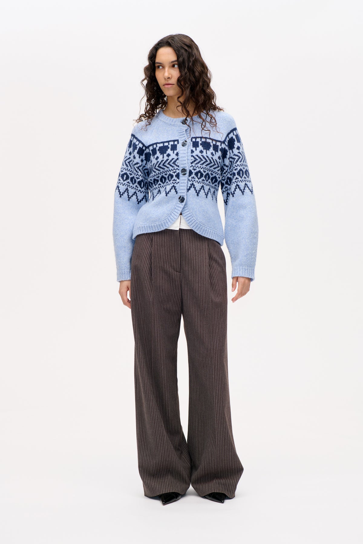 Mannequin portant un cardigan boutonné bleu clair orné de bandes géométriques bleu marine foncé et un pantalon large marron à fines rayures.