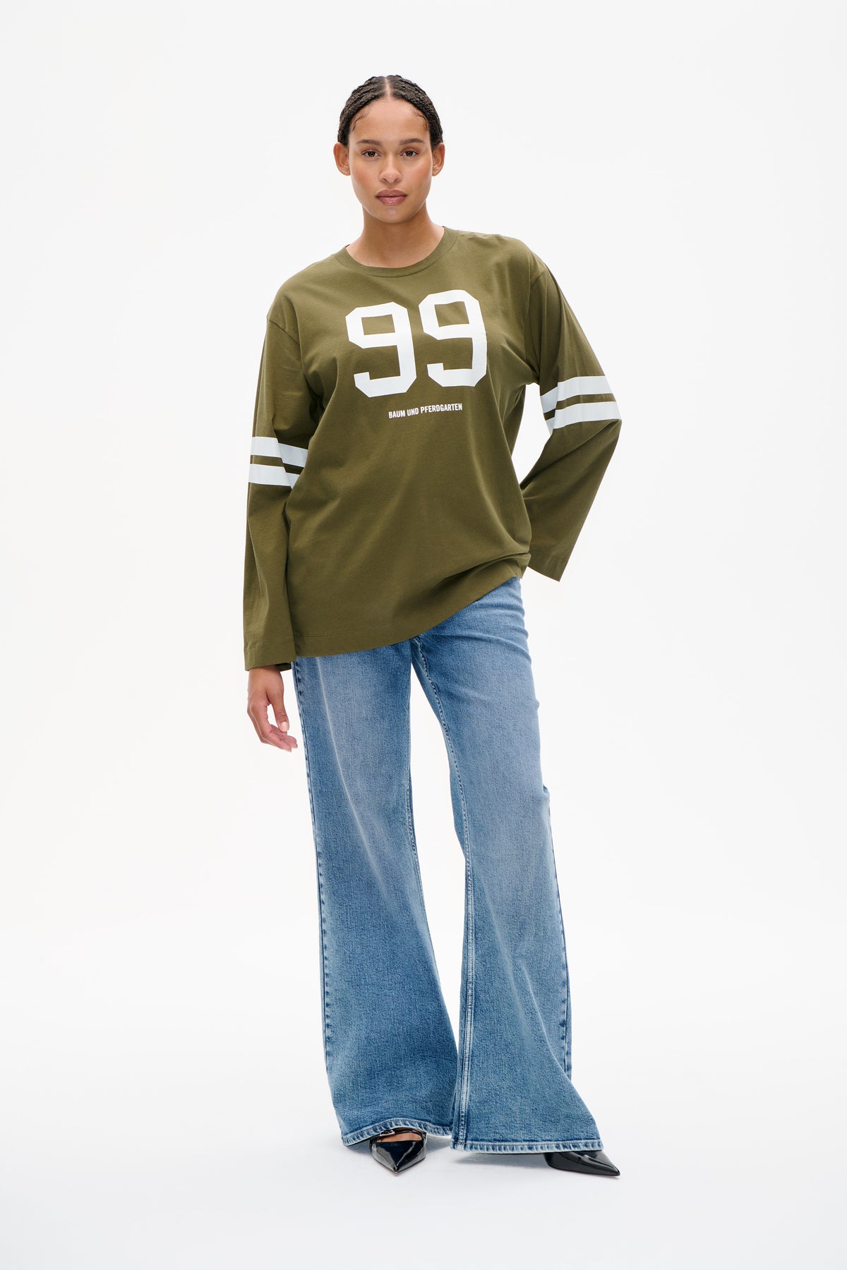 Mannequin portant un T-shirt à manches longues vert olive avec un grand 99 blanc et des manches rayées, associé à un jean large délavé clair.