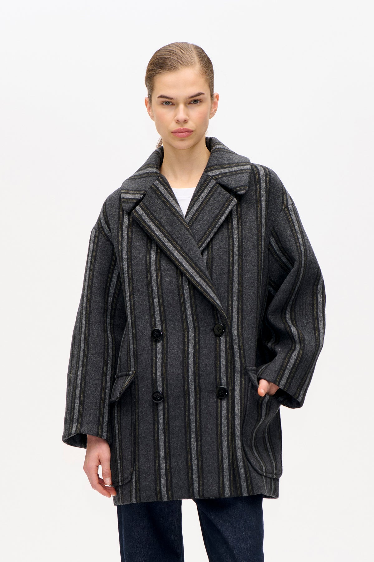 Front view of a model wearing a charcoal grey double-breasted coat with fine vertical stripes, wide lapels and flap pockets.