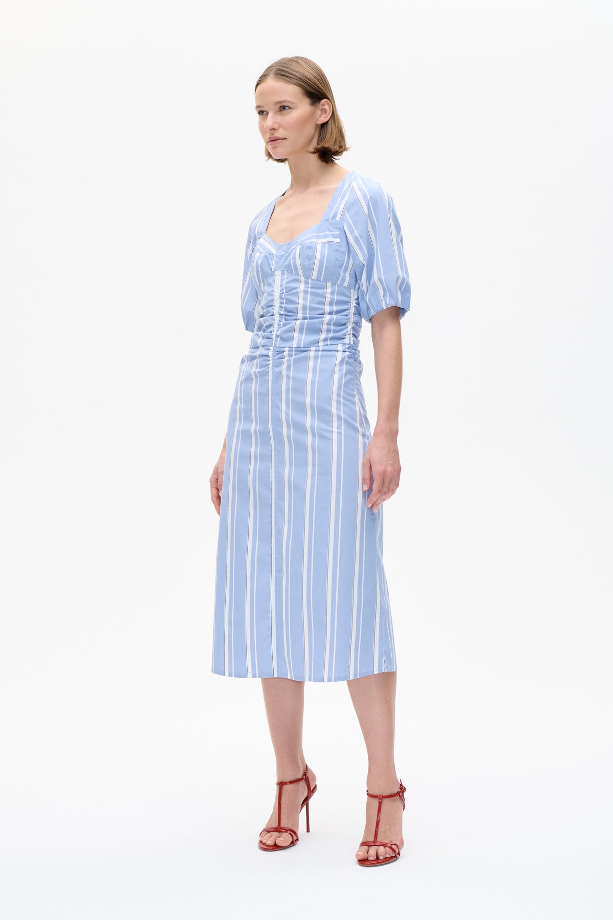 Model wearing a light blue dress with white vertical stripes, a square neckline, short puff sleeves and a fitted ruched bodice.