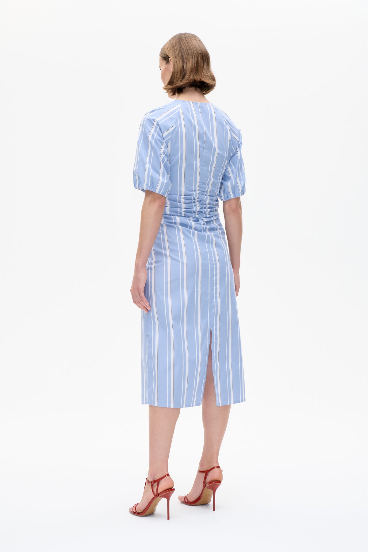 Vue de dos d'une robe bleu clair à rayures verticales blanches, manches bouffantes, taille froncée et fente sur la jupe.