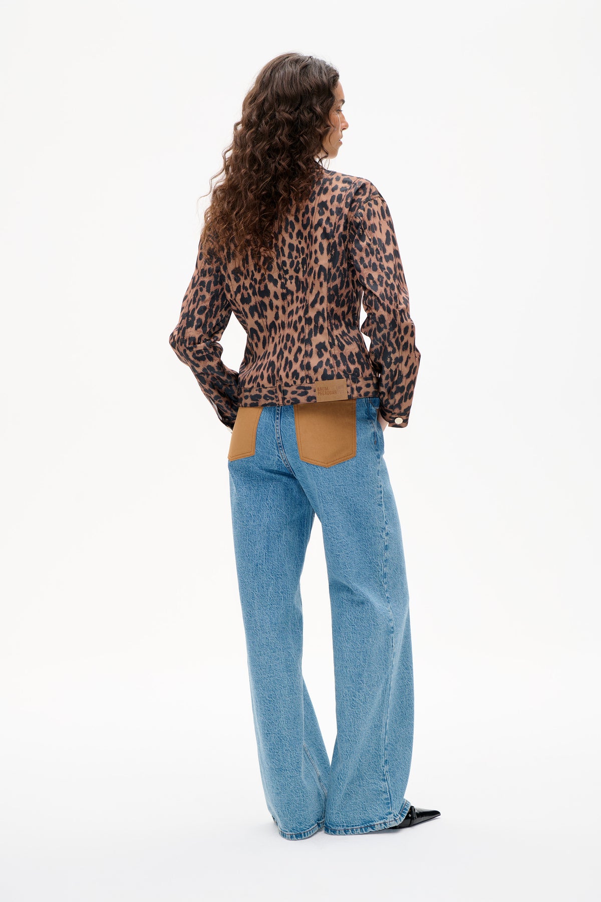 Back view of a brown and black leopard-print jacket with tan patch details, worn with blue jeans.