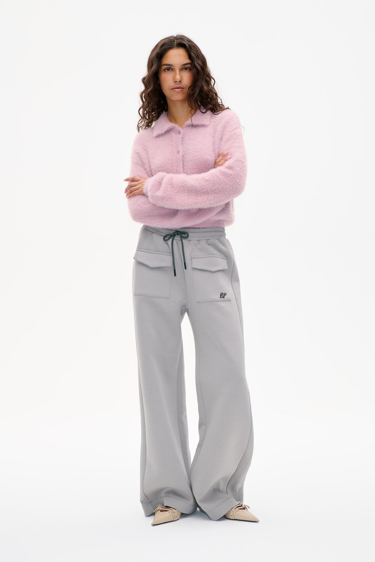 Model wearing a fluffy pale pink collared cardigan and grey wide-leg drawstring trousers with front patch pockets against a white background.