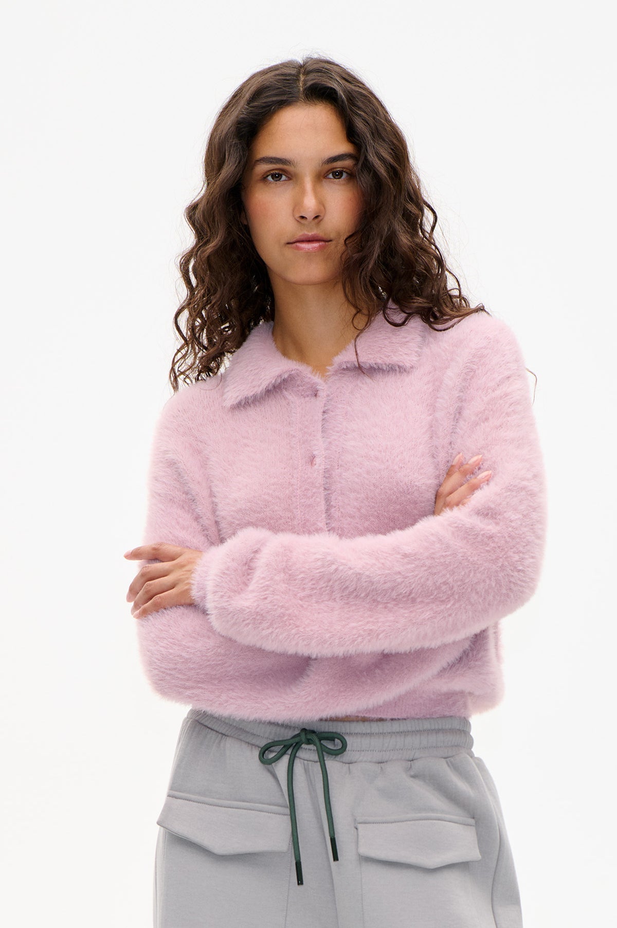 Front view of a model wearing a fuzzy pale pink cardigan with tonal mauve bands and light grey drawstring trousers.