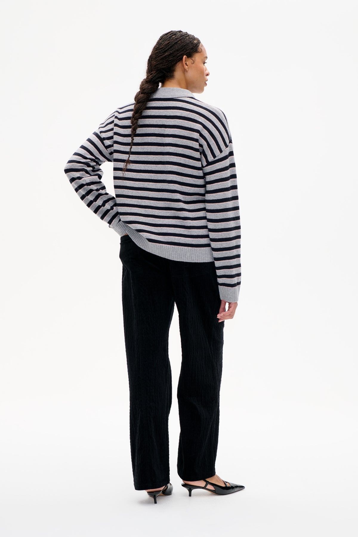 Back view of a model wearing a grey knit sweater with navy and pale pink horizontal stripes and a wide collar.
