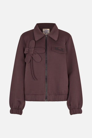 Front view of a plum zip-front jacket with a pointed collar, elasticated cuffs and hem, a fabric flower appliqué and chest patch.