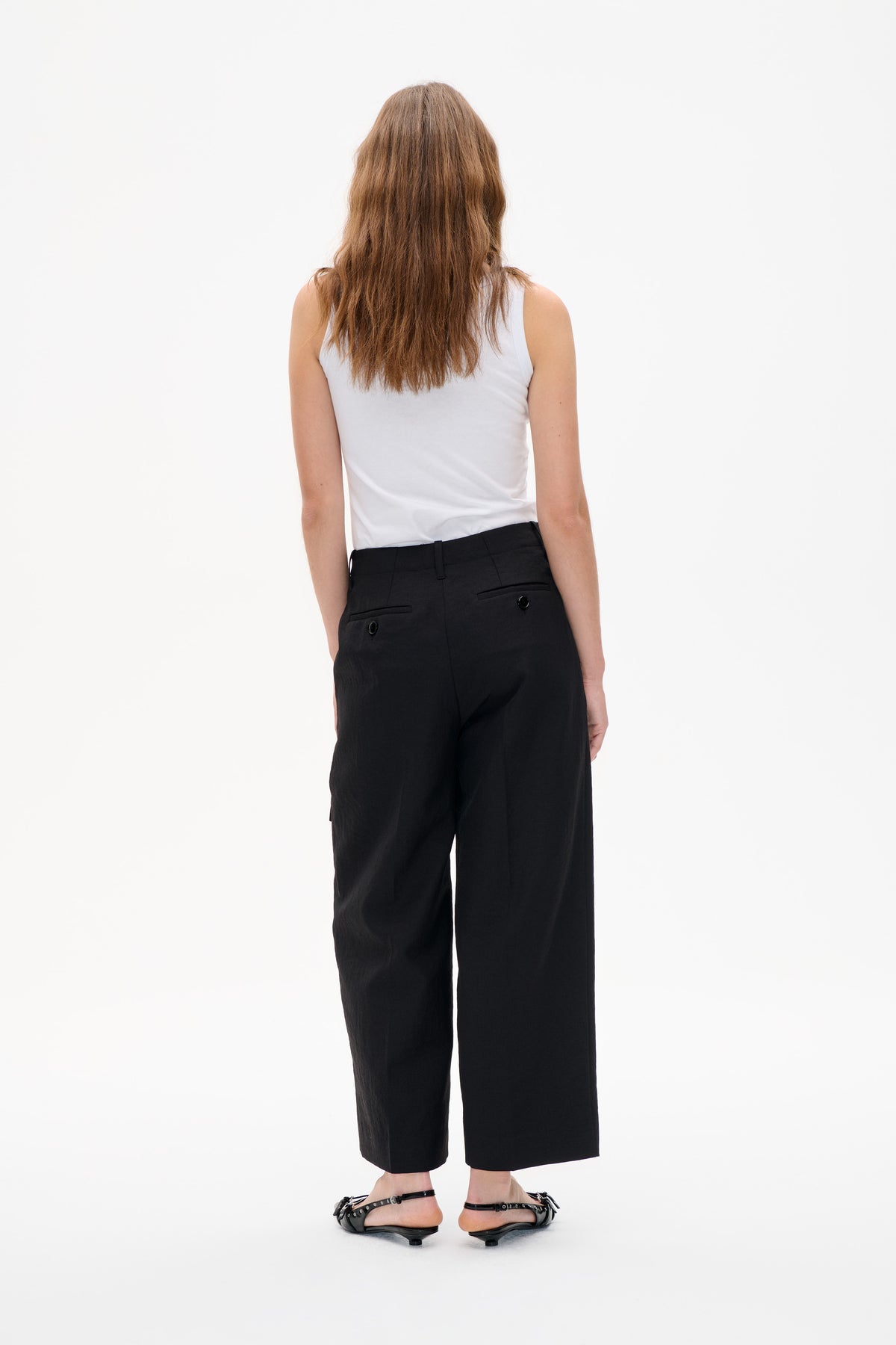 Rear view of a model wearing a plain white sleeveless top, black cropped wide-leg trousers with welt pockets, and black strappy flats.