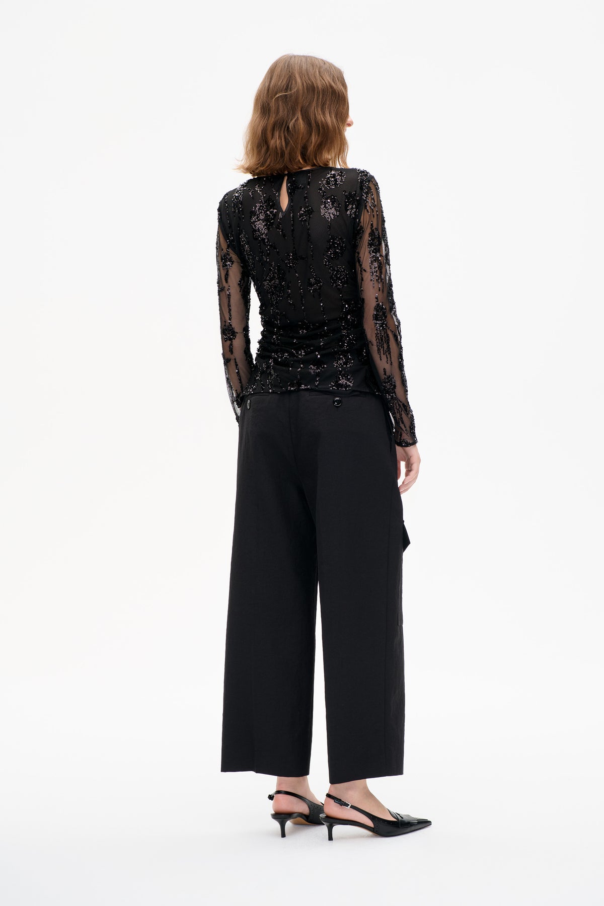 Back view of a sheer black long-sleeve top with scattered sequined floral motifs and a small keyhole opening.