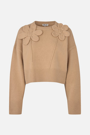 Vorderansicht eines beigen Strickpullovers mit langen Ärmeln, gerippten Bündchen und zwei großen, erhabenen Blumenapplikationen auf den Schultern.