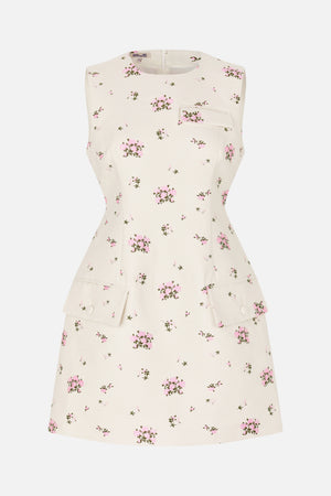 Front view of a cream sleeveless dress with a fitted waist, scattered pink floral print, chest pocket and two flap pockets.