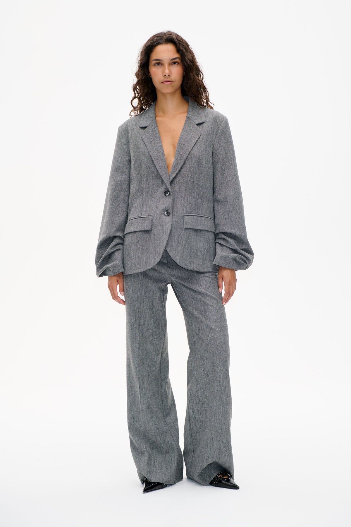 Front view of a model wearing a grey subtly patterned suit with a buttoned blazer, voluminous sleeves and wide-leg trousers.