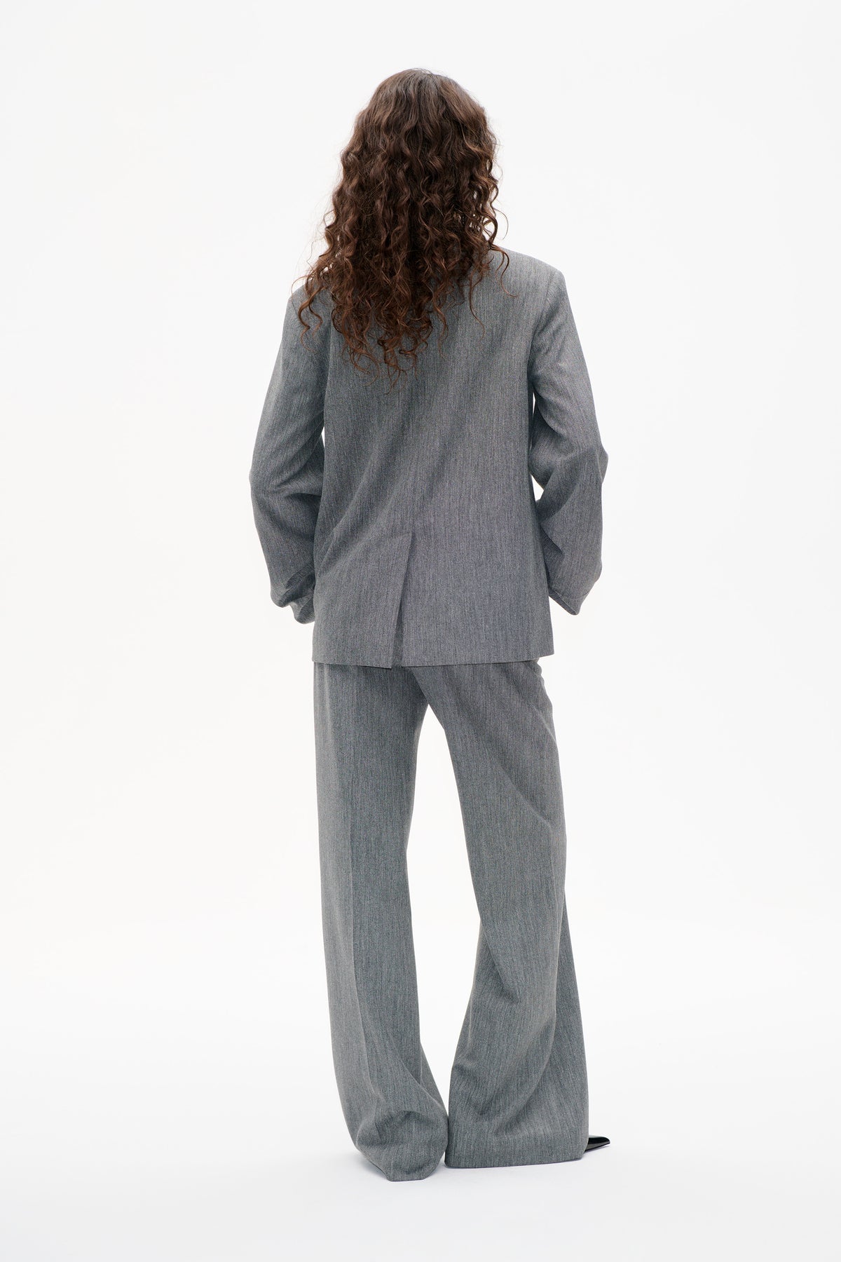 Back view of a model wearing a grey textured blazer with matching wide-leg trousers.