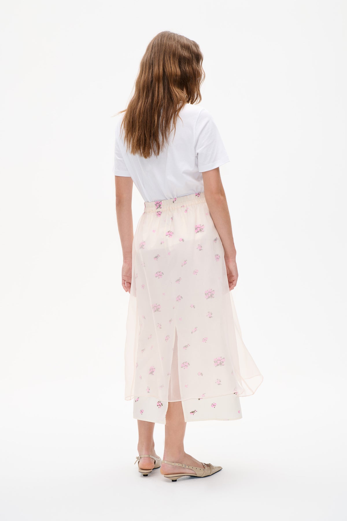 Back view of a model wearing a white short-sleeved T-shirt and an ivory midi skirt with pink floral print and sheer layered panels.