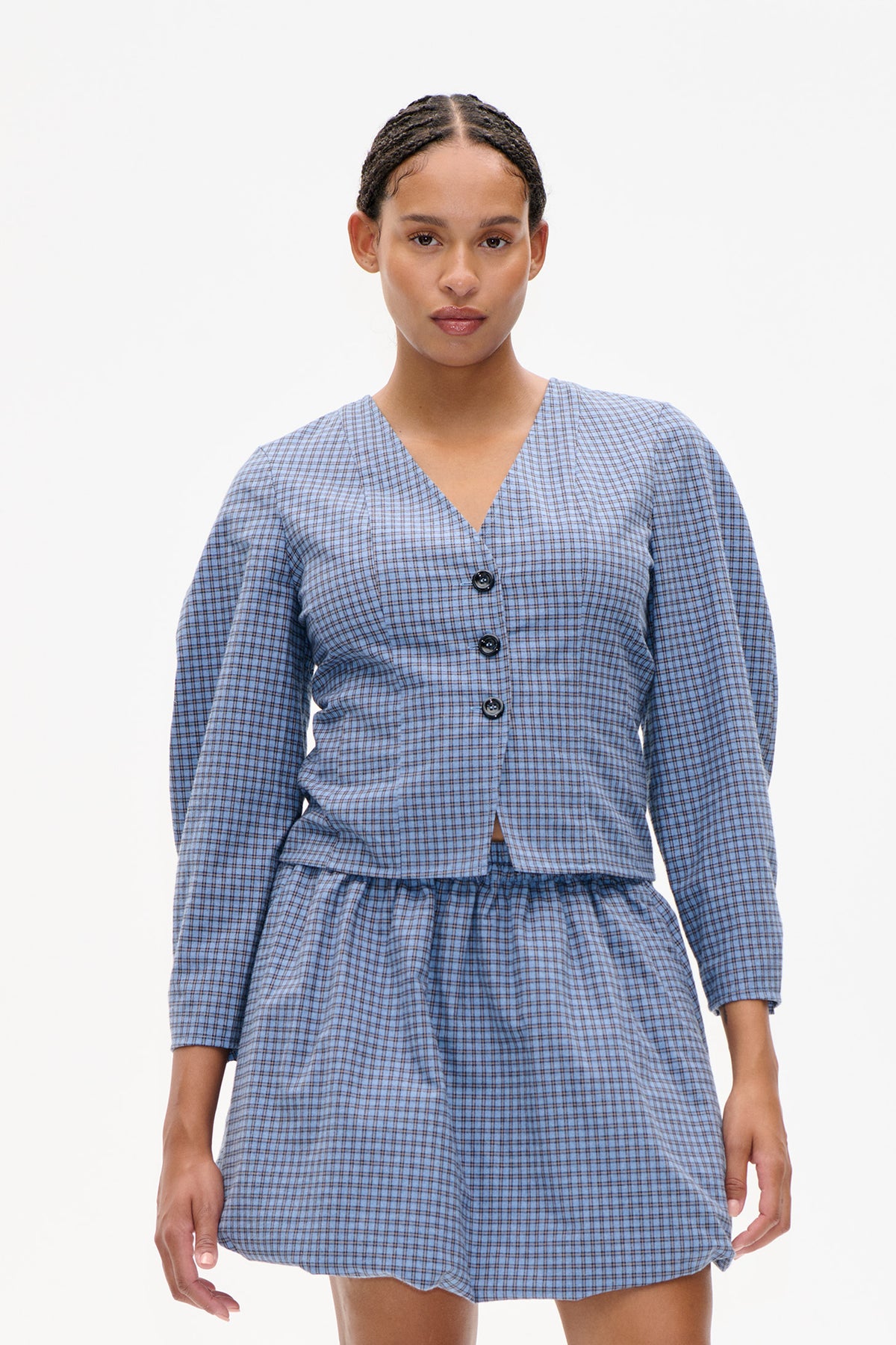 Front view of a light blue checked, V-neck button-front blouse with long sleeves and a matching skirt.