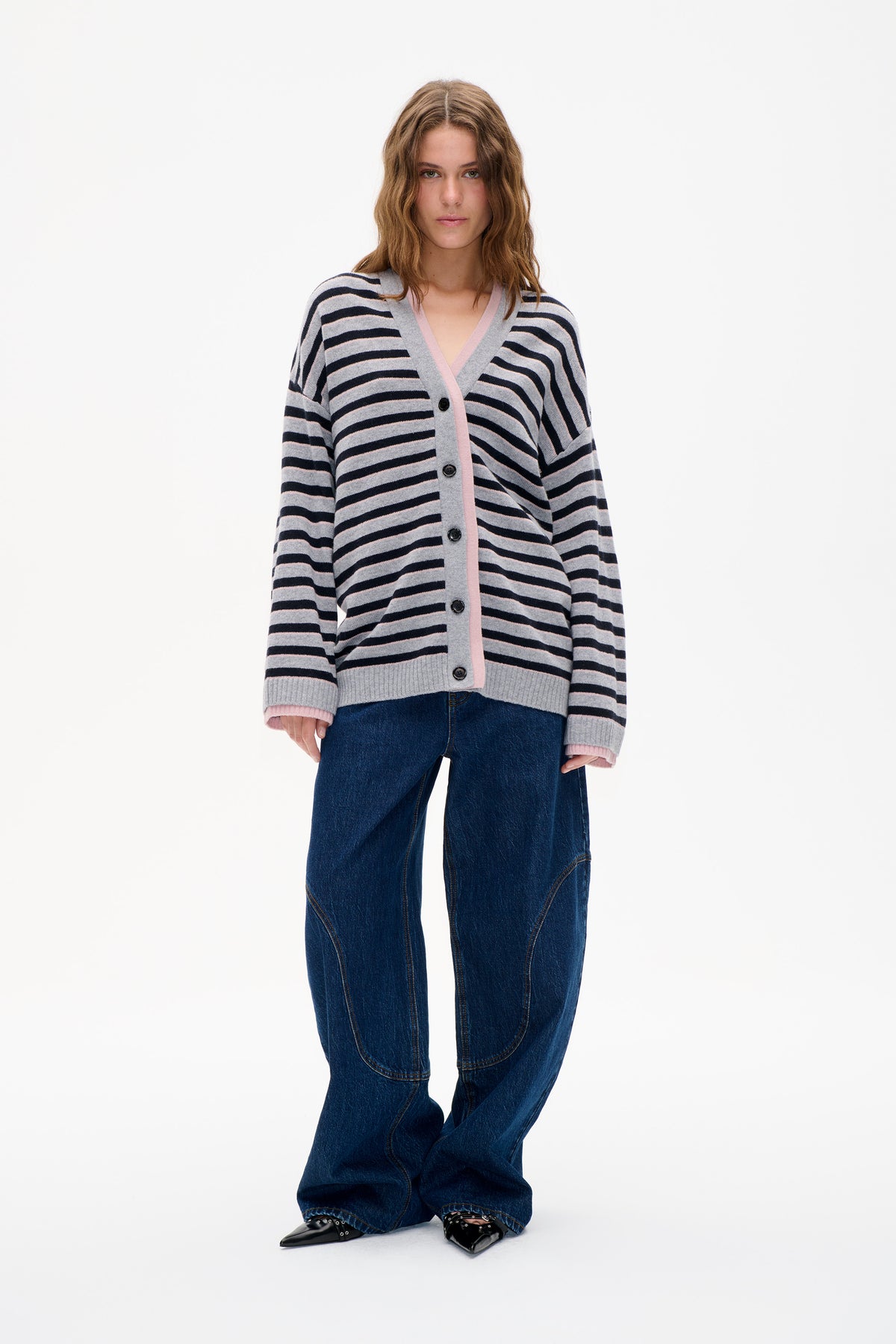 Model wearing a grey V-neck button-front cardigan with navy and pale pink stripes, paired with dark blue jeans.