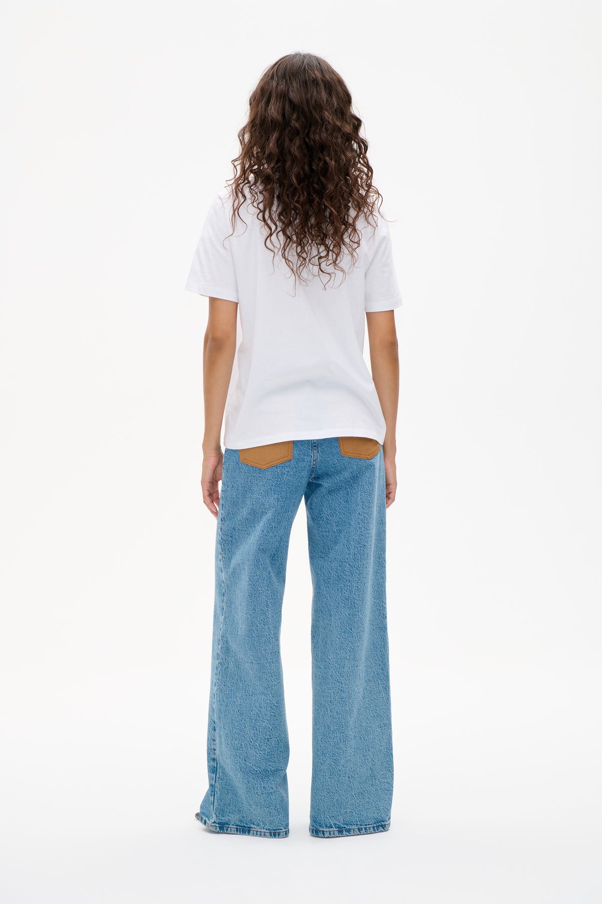 Back view of a model wearing a plain white short-sleeve T-shirt with light blue wide-leg jeans and tan back pockets.
