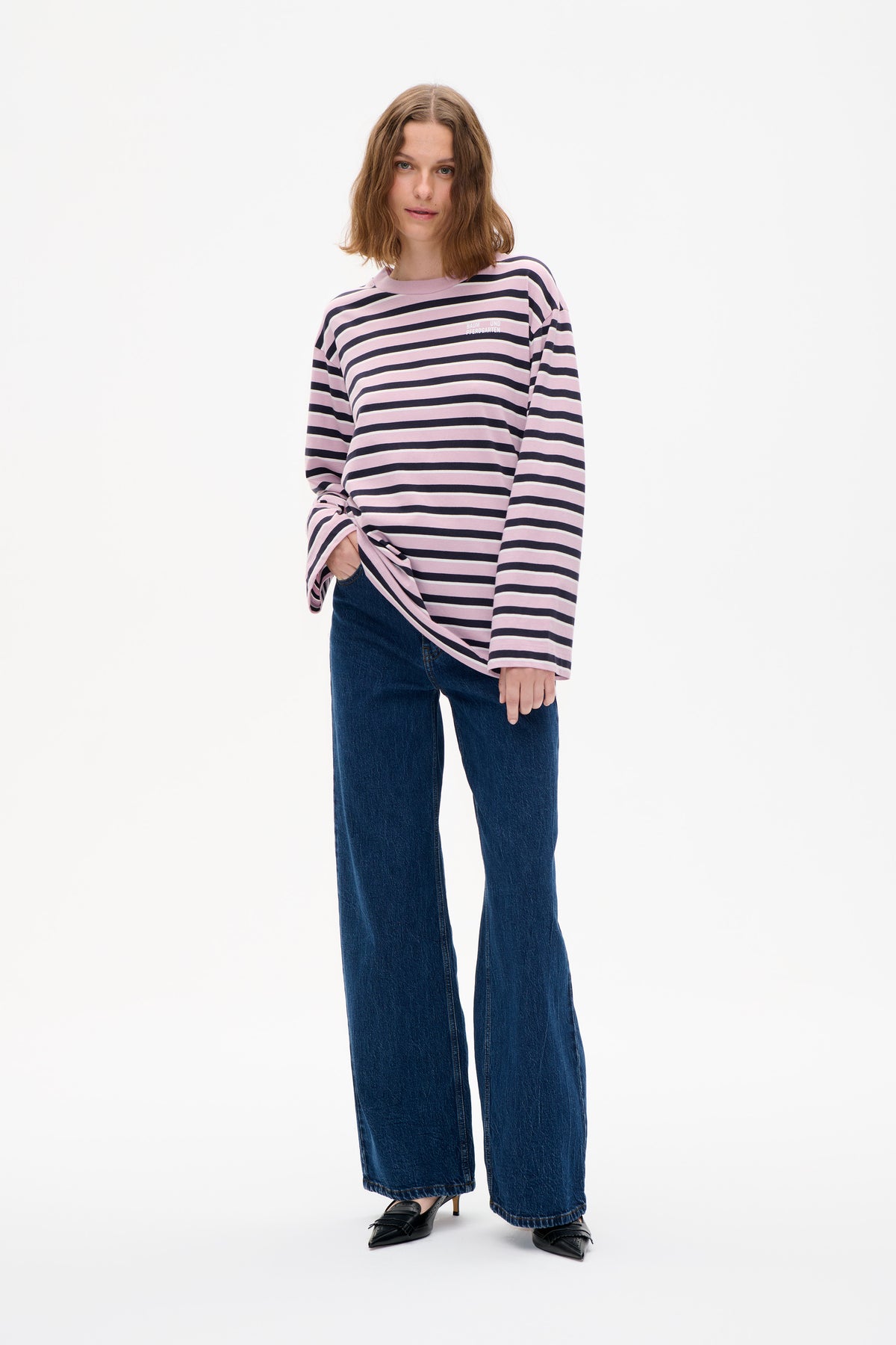 Model draagt een roze top met lange mouwen, marine- en crèmekleurige horizontale strepen en een klein borstlogo, gecombineerd met wijdvallende blauwe jeans.