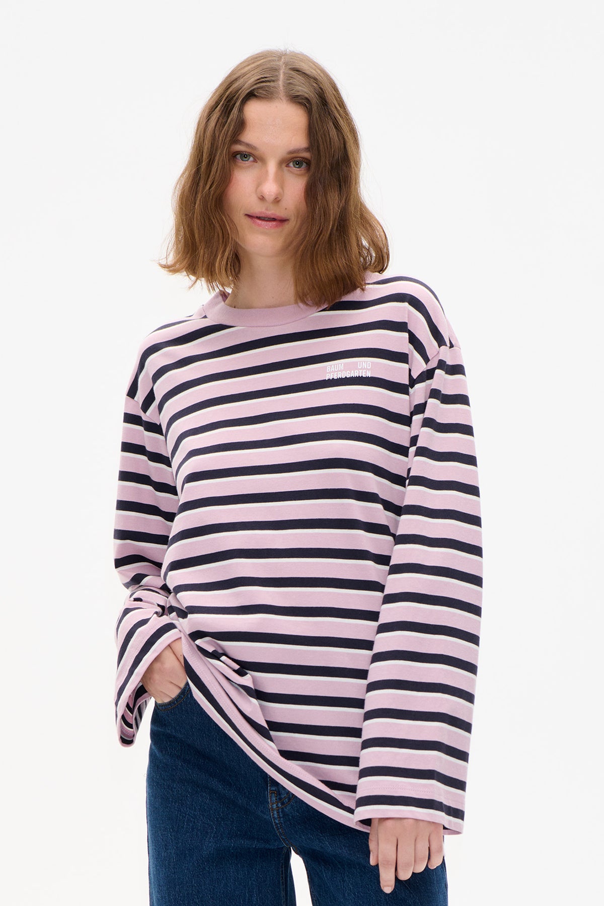 Detailansicht des Vorderteils eines langärmeligen Tops mit horizontalen Streifen in rosa, marineblau und creme und kleinem weißen Logo auf der Brust.