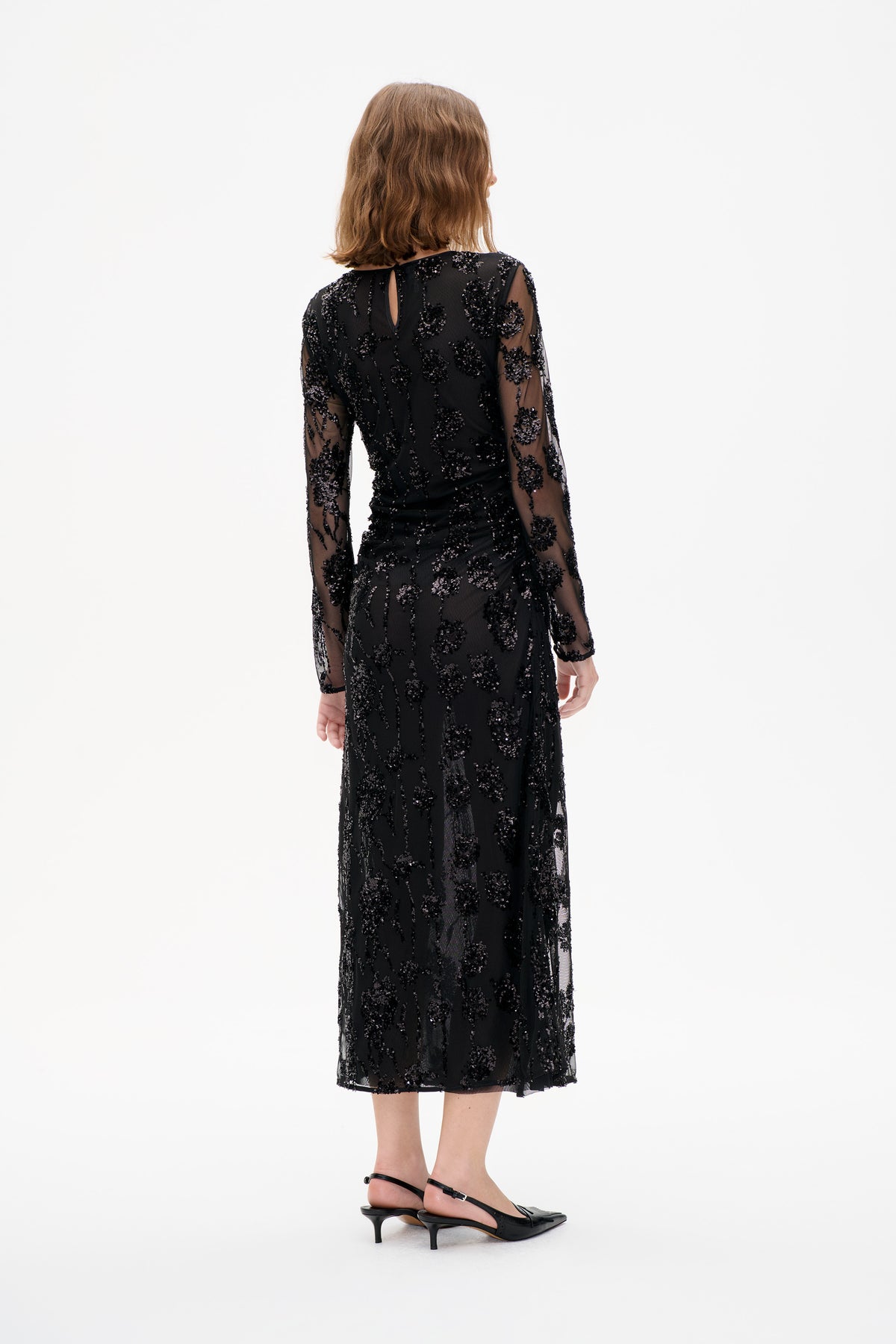 Black sheer long-sleeved midi dress with scattered sequin motifs and a back keyhole, shown from behind on a model.