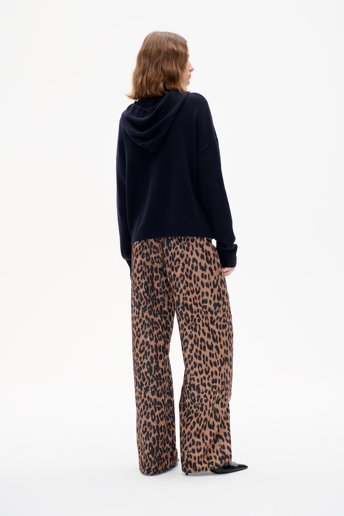 Model viewed from behind wearing a navy hooded sweater and brown-and-black leopard-print wide-leg trousers.