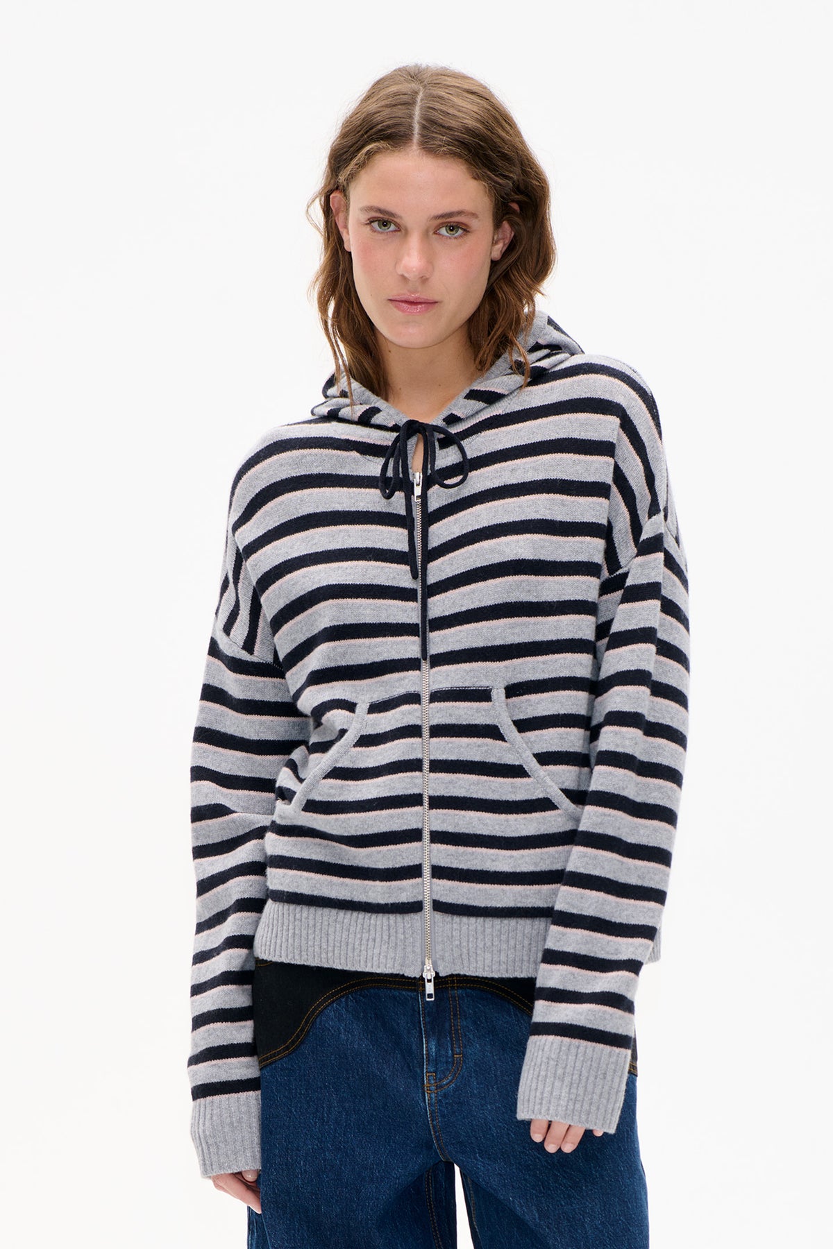 Frontalansicht eines Models, das eine grau-schwarz gestreifte Strickjacke mit Kapuze, Reißverschluss vorne und Kordelzug trägt.