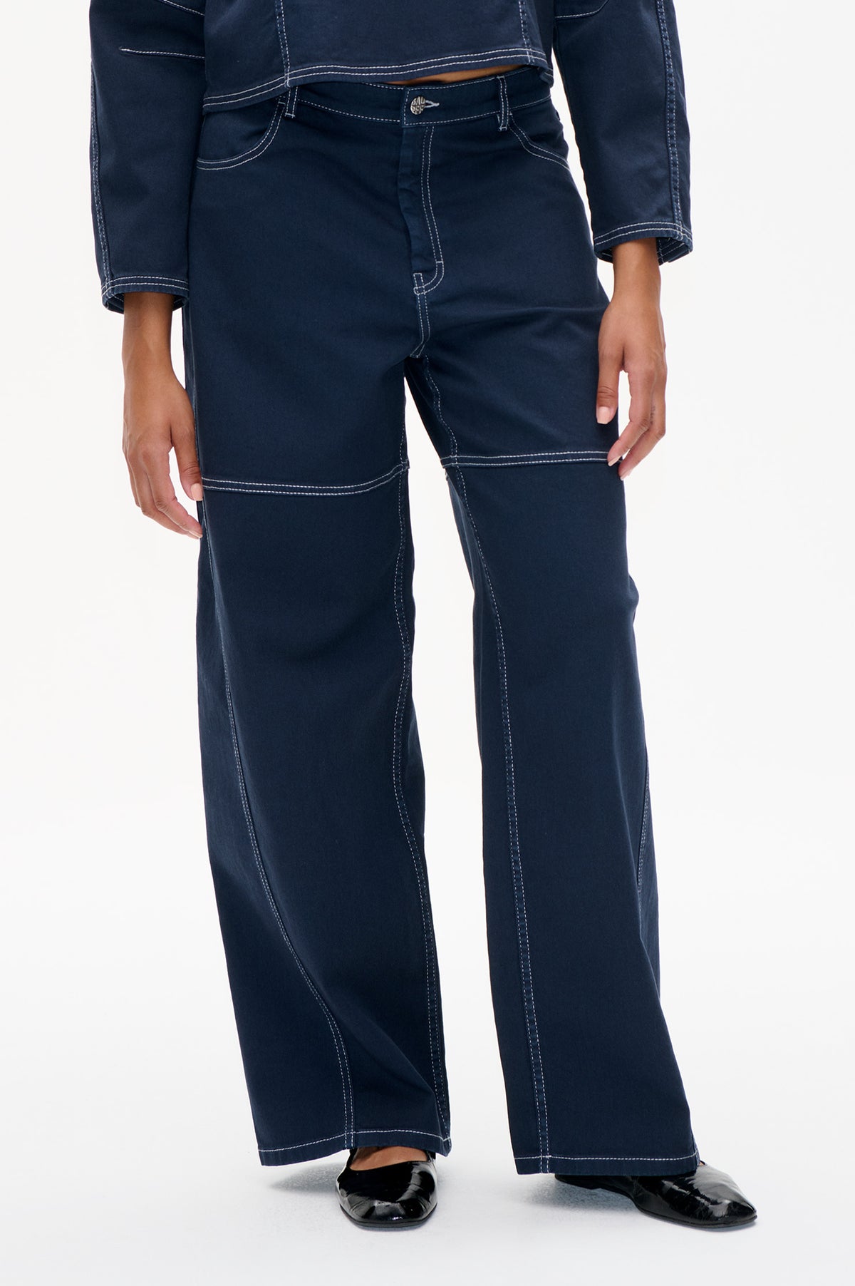 Front detail of dark indigo wide-leg jeans with contrasting white topstitching, shown with a matching cropped jacket.