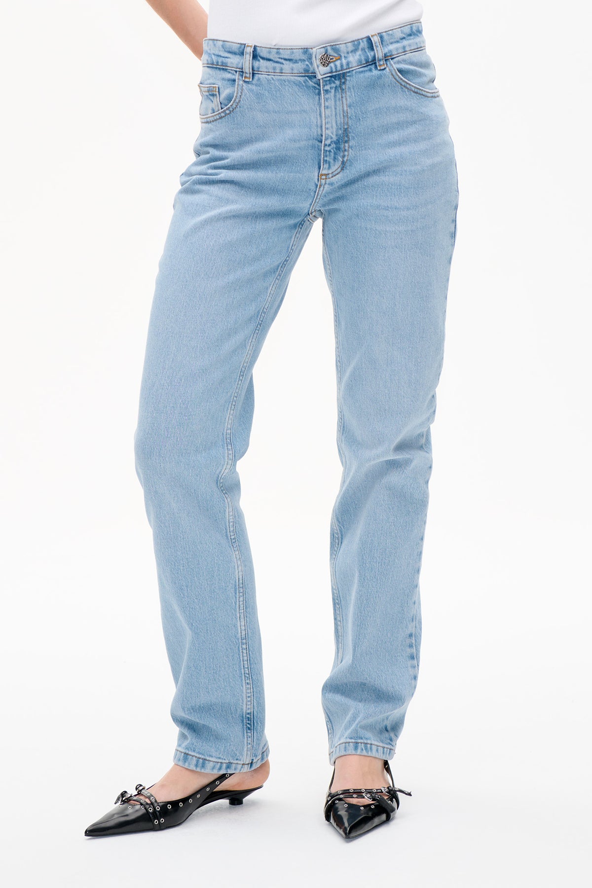 Detailansicht vorne: hellblau gewaschene Jeans mit geradem Bein, Bund mit Knopf und geschwungenen Taschen, kombiniert mit schwarzen, spitzen Flats.